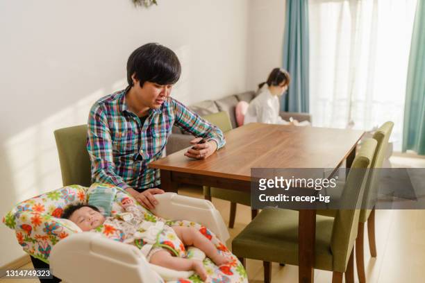 padre cariñoso apoyando a su esposa mientras ella está trabajando en casa en la computadora portátil y el padre cuidando de su bebé recién nacido - balancearse fotografías e imágenes de stock