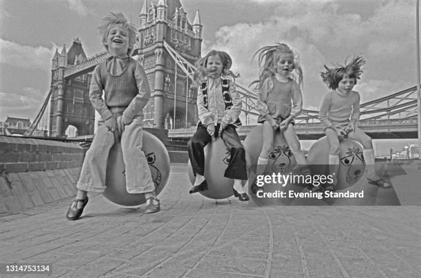 Young David Sammuels and friends bouncing on space hoppers near Tower Bridge in London, UK, 29th July 1974.