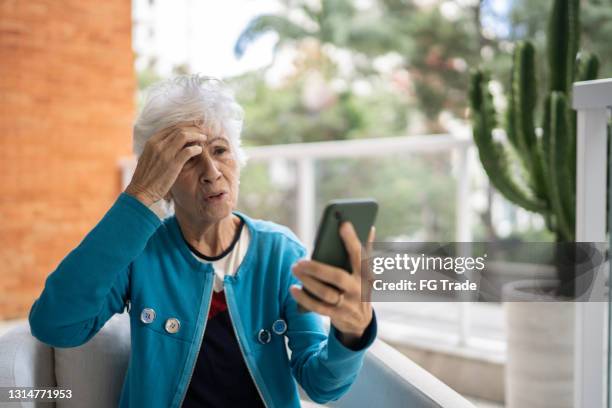 senior woman doing a video call on mobile phone at home - virtual visit stock pictures, royalty-free photos & images