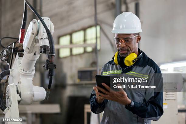 productivity and quality improvement concepts. senior african quality control engineer using touchpad to monitoring robot welding process in engineering part production line. - code 41 stock pictures, royalty-free photos & images