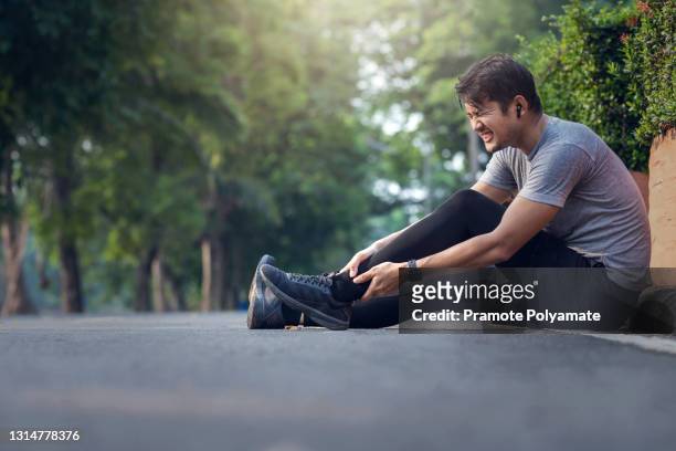asian man achilles injury on running outdoors. man holding achilles tendon by hands close-up and suffering with pain. sprain ligament or achilles tendonitis. - cramp stock pictures, royalty-free photos & images