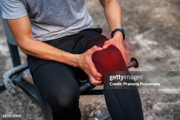 close up of male runner bends over clutching his knee while in intense pain from an acute knee injury while exercising in the park, athletes hurt the knees. the lesion is highlighted in red. - tendon stock pictures, royalty-free photos & images