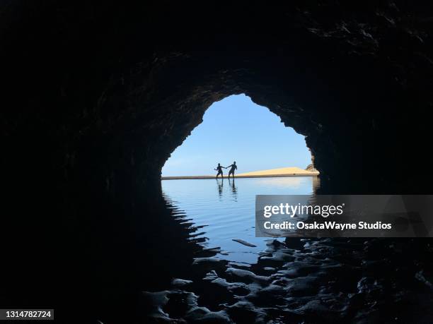 silhouette of two persons standing in rippling shallow water behind tunnel. - kapaa beach park stock pictures, royalty-free photos & images