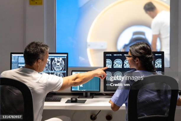 rückansicht von zwei ärzten, die die ergebnisse des mrt-scans analysieren. mann zeigt auf bilder auf dem bildschirm. - back of womens heads stock-fotos und bilder