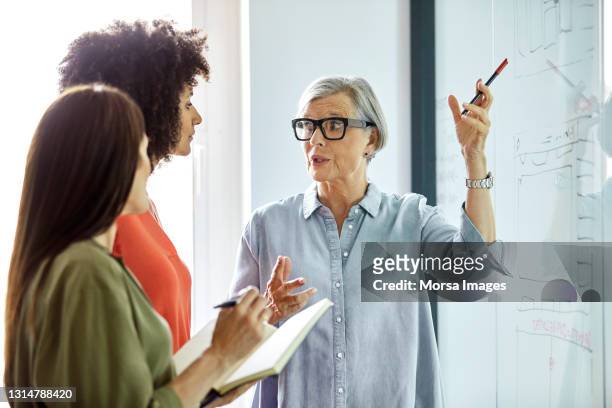 businesswoman explaining strategy to coworkers - leanincollection working women fotografías e imágenes de stock