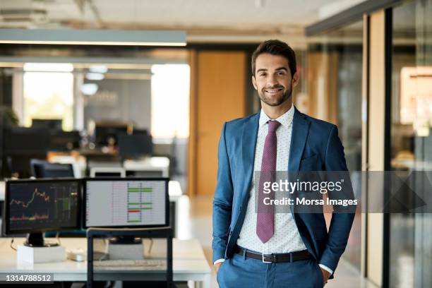 happy businessman with hands in pockets at office - pak stockfoto's en -beelden