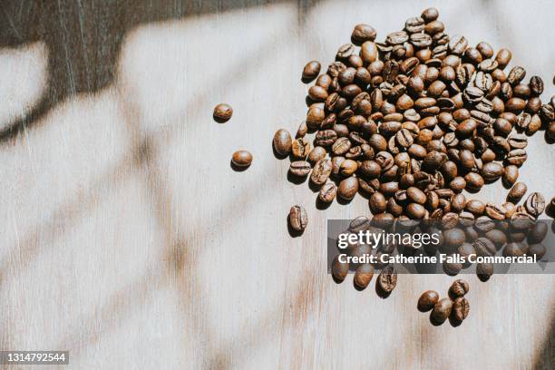 close-up of whole coffee beans on a sunny wooden surface - coffee cups table stock pictures, royalty-free photos & images