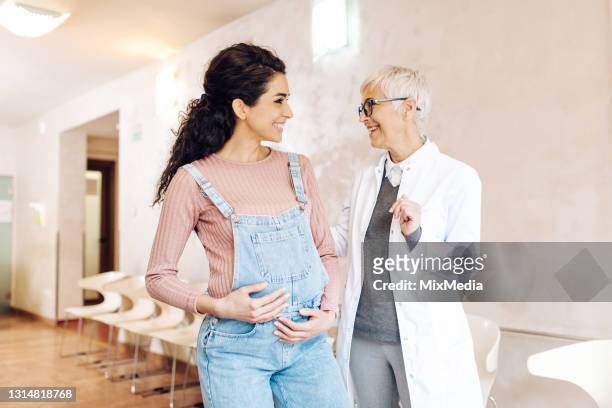 doctor talking with a young woman that expects a baby at the clinic waiting room - pregnancy appointment stock pictures, royalty-free photos & images