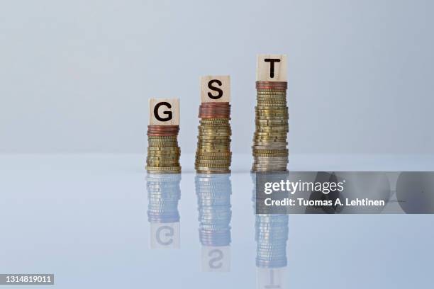 word "gst" on wooden blocks on top of ascending stacks of coins against gray background. - vat imagens e fotografias de stock