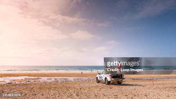 Panoramic view of a RNLI Lifeguard on duty standing on the back of an emergency response vehicle on Fistral Beach in Newquay in Cornwall.