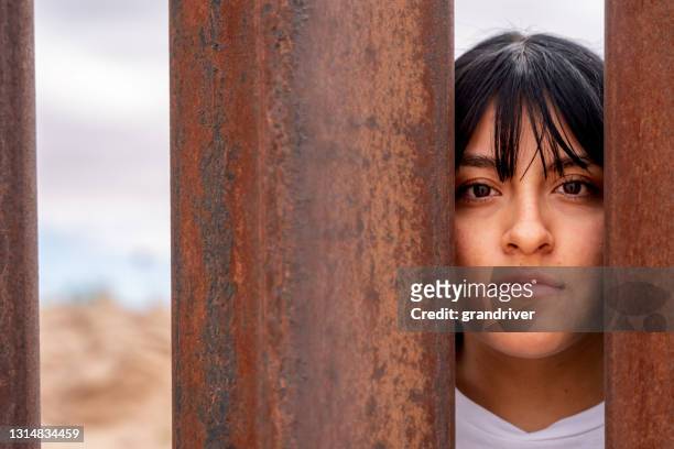 cheerful young mexican woman posing behind the international border barrier wall between the usa and mexico - international organisation for migration stock pictures, royalty-free photos & images