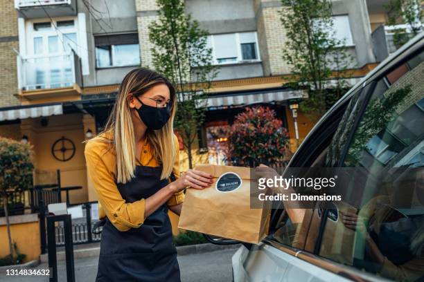 curbside pegar funcionário de restaurante dando sacos de pedidos para o cliente - driving mask - fotografias e filmes do acervo