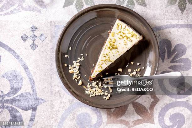 Piece of raw vegan cheesecake. No bake gluten free. Decorated by lime zest and cashew nuts on plate on ornate ceramic table. Sunlight. Flat lay....