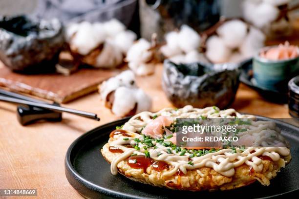 Homemade japanese fast food okonomiyaki cabbage pancake with onion. Pickled ginger. Mayo sauce on black ceramic plate. Chopsticks. Teapot. Cotton....