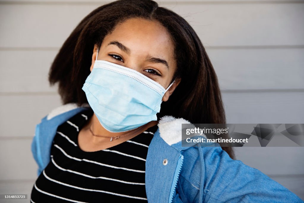 Preteen mixed-race girl smiling behind protective mask outdoors.