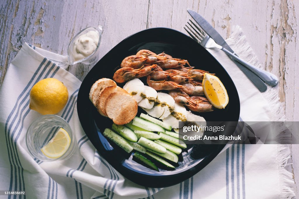 Plate of delicious appetizer: fried shrimp, mozzarella cheese, pesto, fried bread, lemon and cucumber sticks with sauce on gray wooden table.