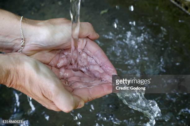 Fresh water flowing from a fountain in the hands of a woman. France.