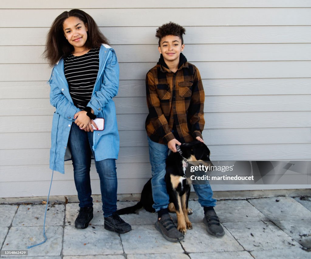 Retrato de hermanos preadolescentes de raza mixta con perro al aire libre.