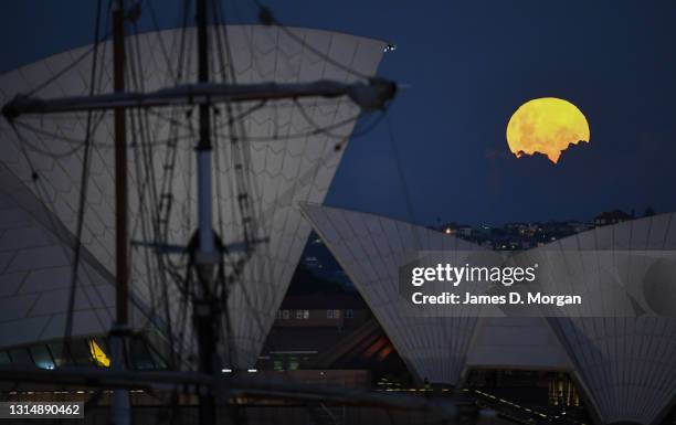 The moon rises behind the Sydney Opera House with a tall ship mast in the foreground on April 27, 2021 in Sydney, Australia. The pink super moon is...