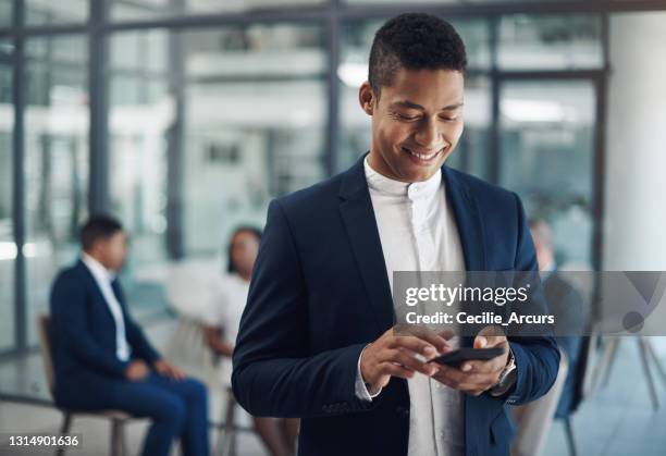 scatto di un giovane uomo d'affari che usa un cellulare in un ufficio con i suoi colleghi sullo sfondo - man suit using phone tablet foto e immagini stock