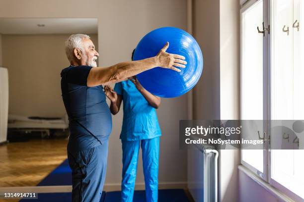 senior man exercising with a female african-american physiotherapist - fitness ball imagens e fotografias de stock