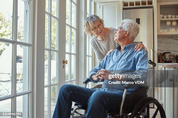 shot of a senior man sitting in his wheelchair while bonding with his wife at home - husband stock pictures, royalty-free photos & images