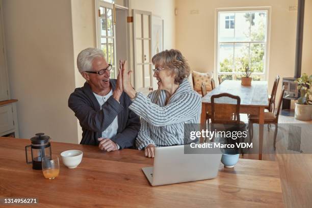 shot of a senior couple giving each other a high five while using a laptop at home - legislation stock pictures, royalty-free photos & images