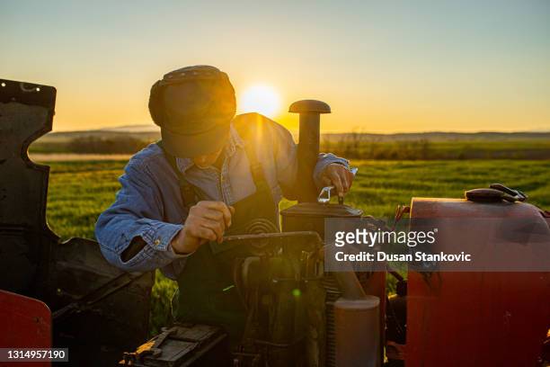 older farmer repairing agricultural equipment on a farm during sunset - tractor repair stock pictures, royalty-free photos & images