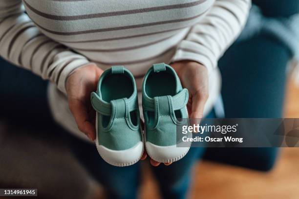 midsection of pregnant woman holding a pair of baby shoes in front of her belly - baby boot stock pictures, royalty-free photos & images