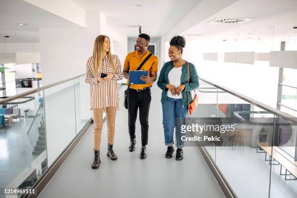 business professionals talking while walking in office corridor - business friendship stock pictures, royalty-free photos & images