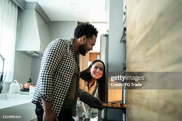 couple looking bake food preparation into the oven at home - man baking cookies stock pictures, royalty-free photos & images