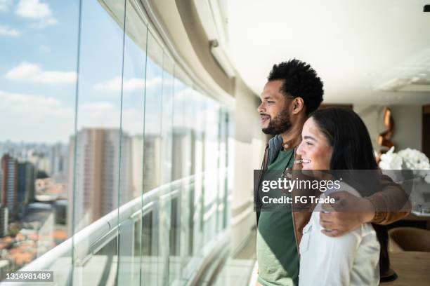 seitenansicht des paares, das durch das fenster der neuen wohnung des erben schaut - super rich stock-fotos und bilder