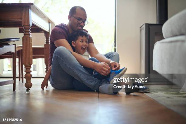 ontsproten van een vaderzitting op de vloer met zijn zoon die zijn schoenveters thuis vastmakert - school tie stockfoto's en -beelden