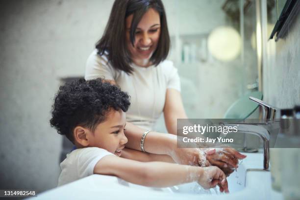 ontsproten van een jonge jongen en zijn moeder die hun handen in de badkamersgootsteen thuis wassen - child washing hands stockfoto's en -beelden