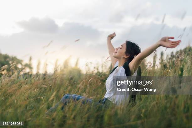 young woman enjoying nature, sitting in meadow - arms outstretched stock pictures, royalty-free photos & images