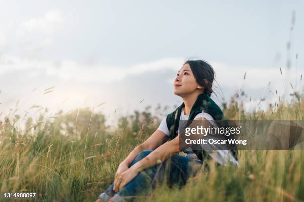 young woman enjoying nature, sitting in meadow - woman relaxation stock pictures, royalty-free photos & images