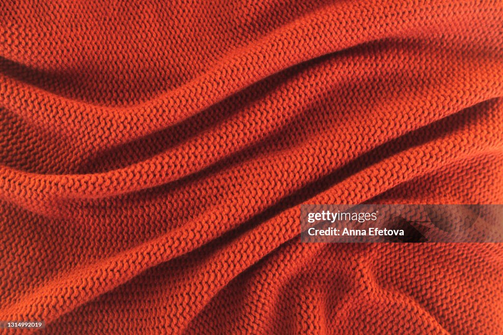 Texture of knitted red sweater folded in a swirling pattern. Flat lay style, close-up.