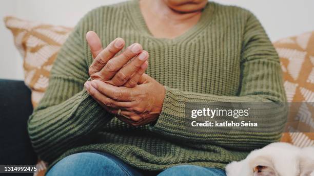 projectile recadré d’une femme aînée méconnaissable frottant ses mains tout en s’asseyant sur le sofa dans son appartement avec son chat à côté d’elle - arthritis hands photos et images de collection