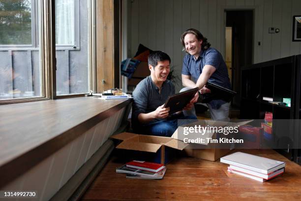 male couple in living room unpacking boxes and looking at picture frame, candid - memories box stock pictures, royalty-free photos & images