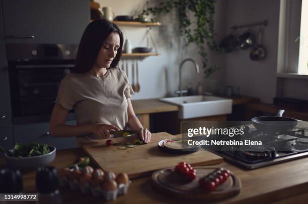 a beautiful young girl with long hair in light clothes is slicing avocado with a knife to prepare a delicious breakfast. breakfast at home. - long table stockfoto's en -beelden