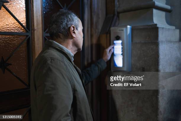 senior man ringing an intercom of a city house late at night - going home night stock-fotos und bilder