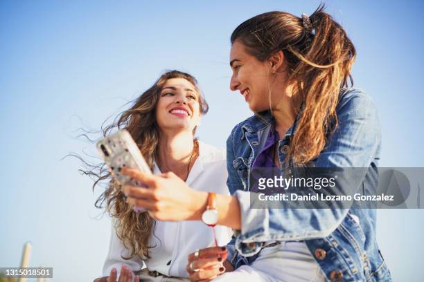 women couple using phone - friends sharing mediterranean fotografías e imágenes de stock