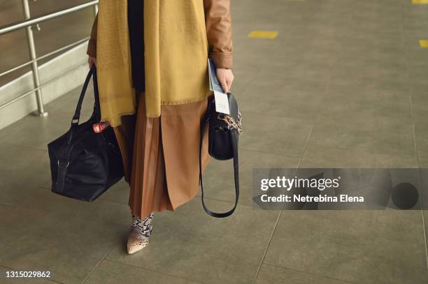 a business-like rich woman traveling with a travel bag holds a passport and a flight ticket. female legs, close-up. business trip. travel concept - woman flying scarf stock pictures, royalty-free photos & images