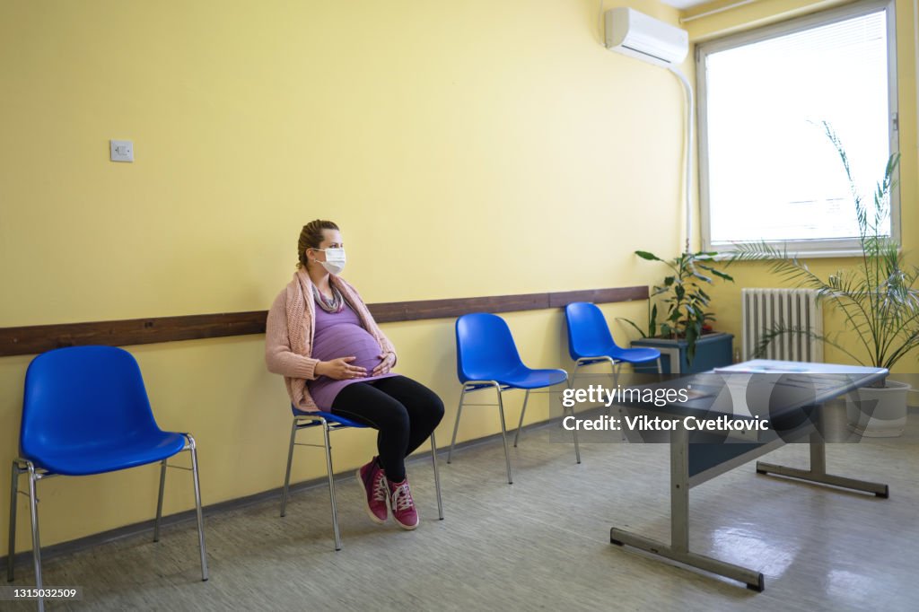 Une jeune femme enceinte avec un masque de protection dans la salle d’attente