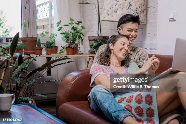 lesbian couple spooning on sofa while watching laptop - real wife sharing 個照片及圖片檔