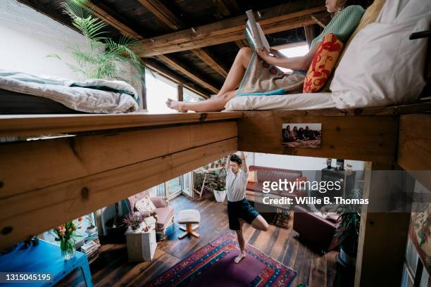 woman reading on mezzanine while partner stretches downstairs - mezzanine stockfoto's en -beelden