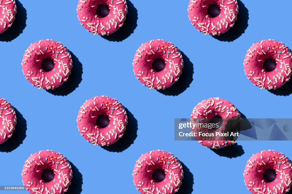 Pink doughnut on pastel blue background. Chewed donut.
