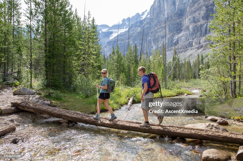 Hikers cross a mountain stream on a log