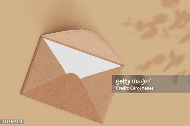 opened brown envelope with blank card on beige background and shadow - brown envelope stock pictures, royalty-free photos & images