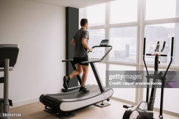 caucasian adult man running on a treadmill in the gym next to a large window - man gym face mask stock pictures, royalty-free photos & images